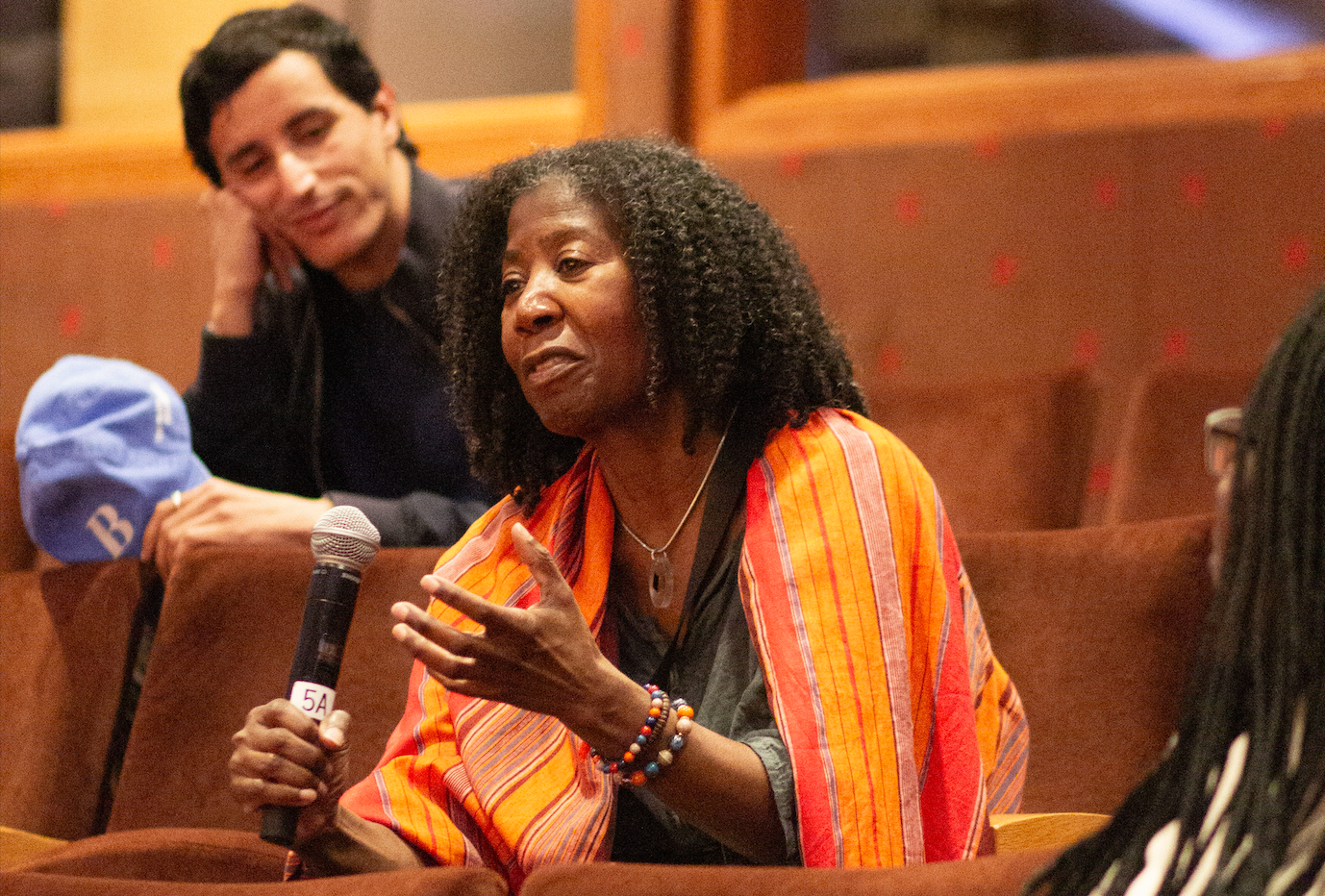 An older black woman, holding a microphone, asks Alice Diop a question during the Q+A portion of the event.
